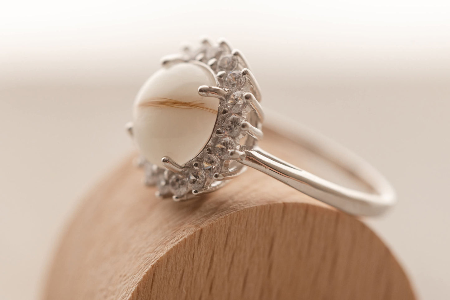 Bague souvenir avec un superbe cabochon de lait maternel et mèche de cheveux de bébé, entourée de strass étincellantes. 