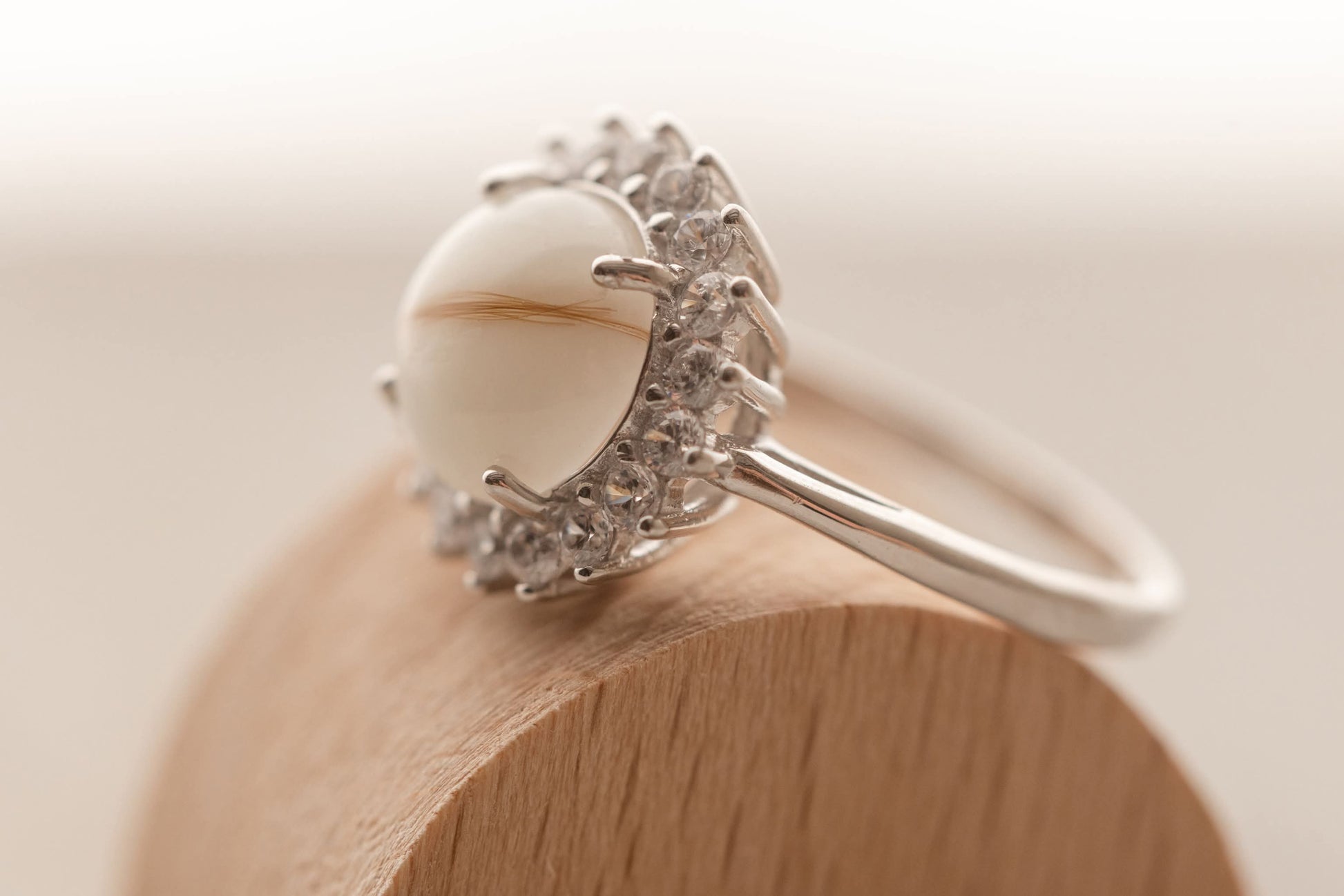 Bague souvenir avec un superbe cabochon de lait maternel et mèche de cheveux de bébé, entourée de strass étincellantes. 