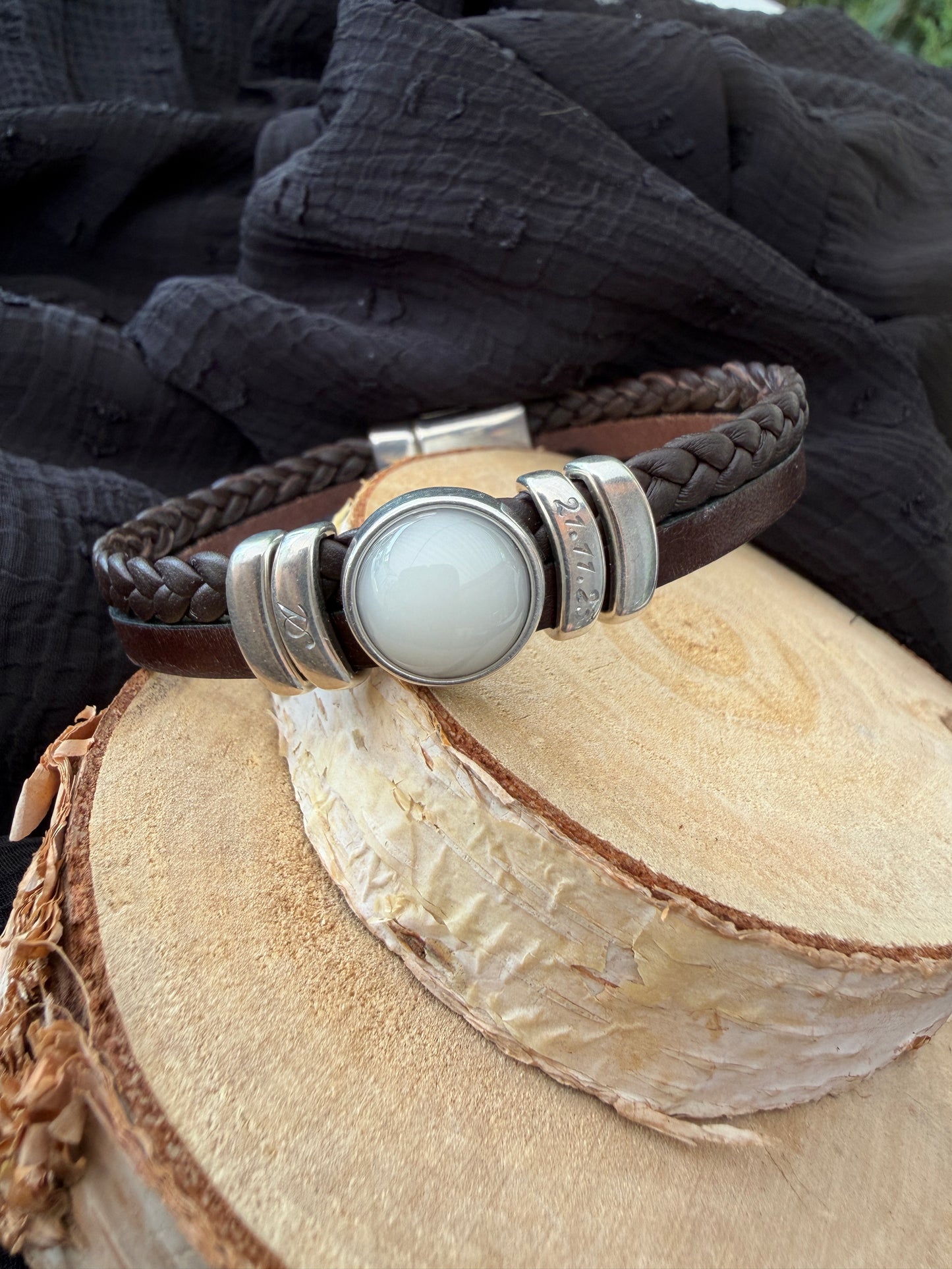 Bracelet en cuir brun contenant une pierre de lait maternel et la gravure de l'initial et la date de naissance de bébé. 