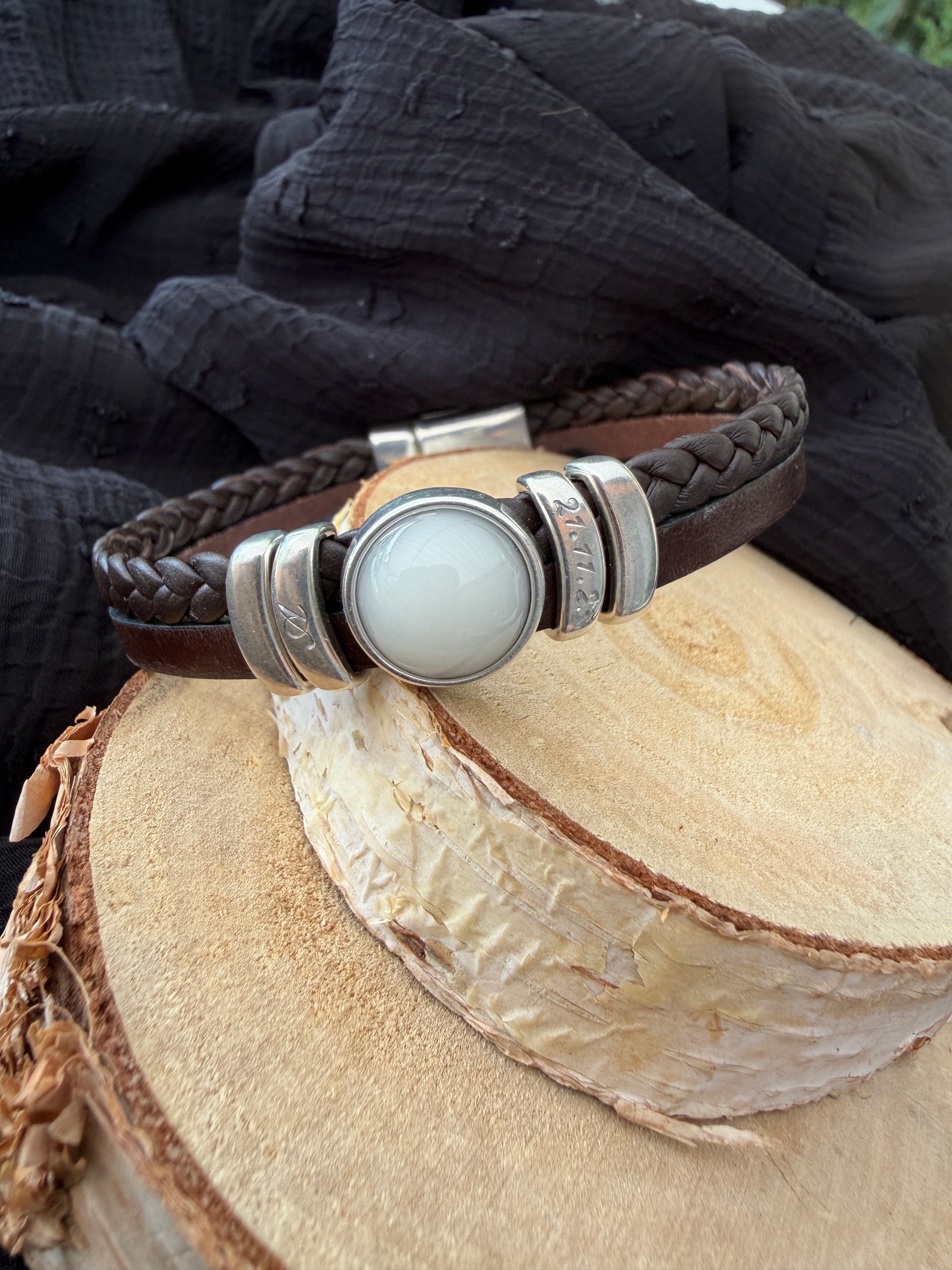 Bracelet en cuir brun contenant une pierre de lait maternel et la gravure de l'initial et la date de naissance de bébé. 